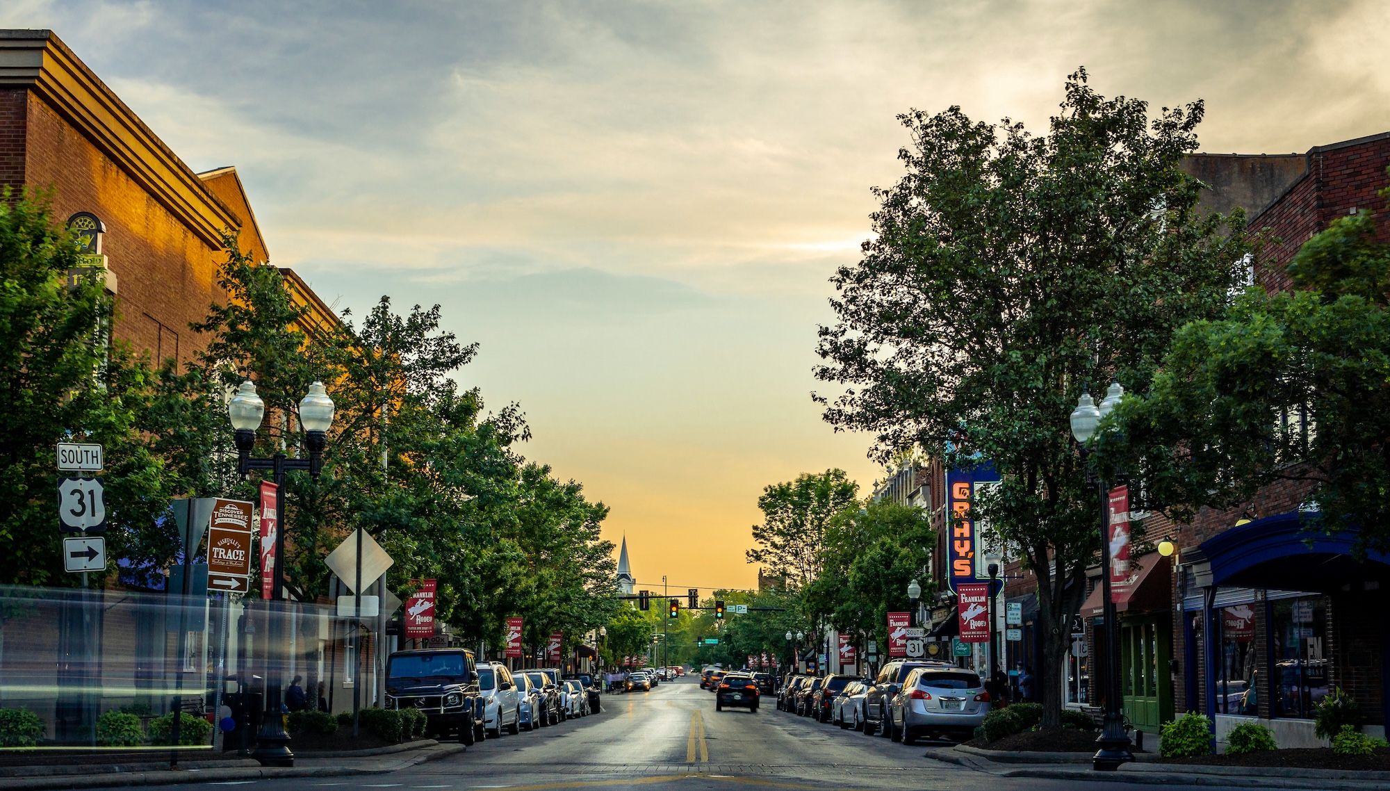 View of the downtown with sunset in the background, trees and cars on each side.